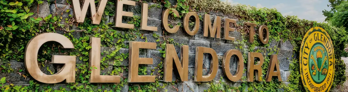 The Welcome to Glendora monument sign, bronze letters on an ivy-covered stone wall beside the City of Glendora seal